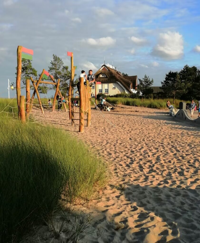 Blick auf einen Strandspielplatz mit Holzspielgeräten und Reeddachhaus in Dahme Norddeutschland